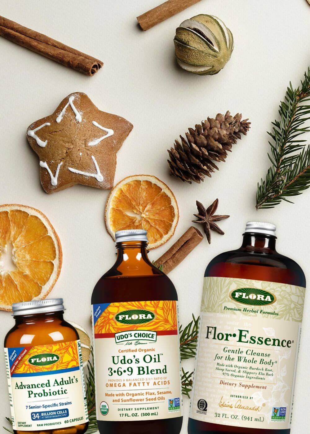 Three Flora product bottles on a festive background with cinnamon sticks, oranges, and pine cones.
