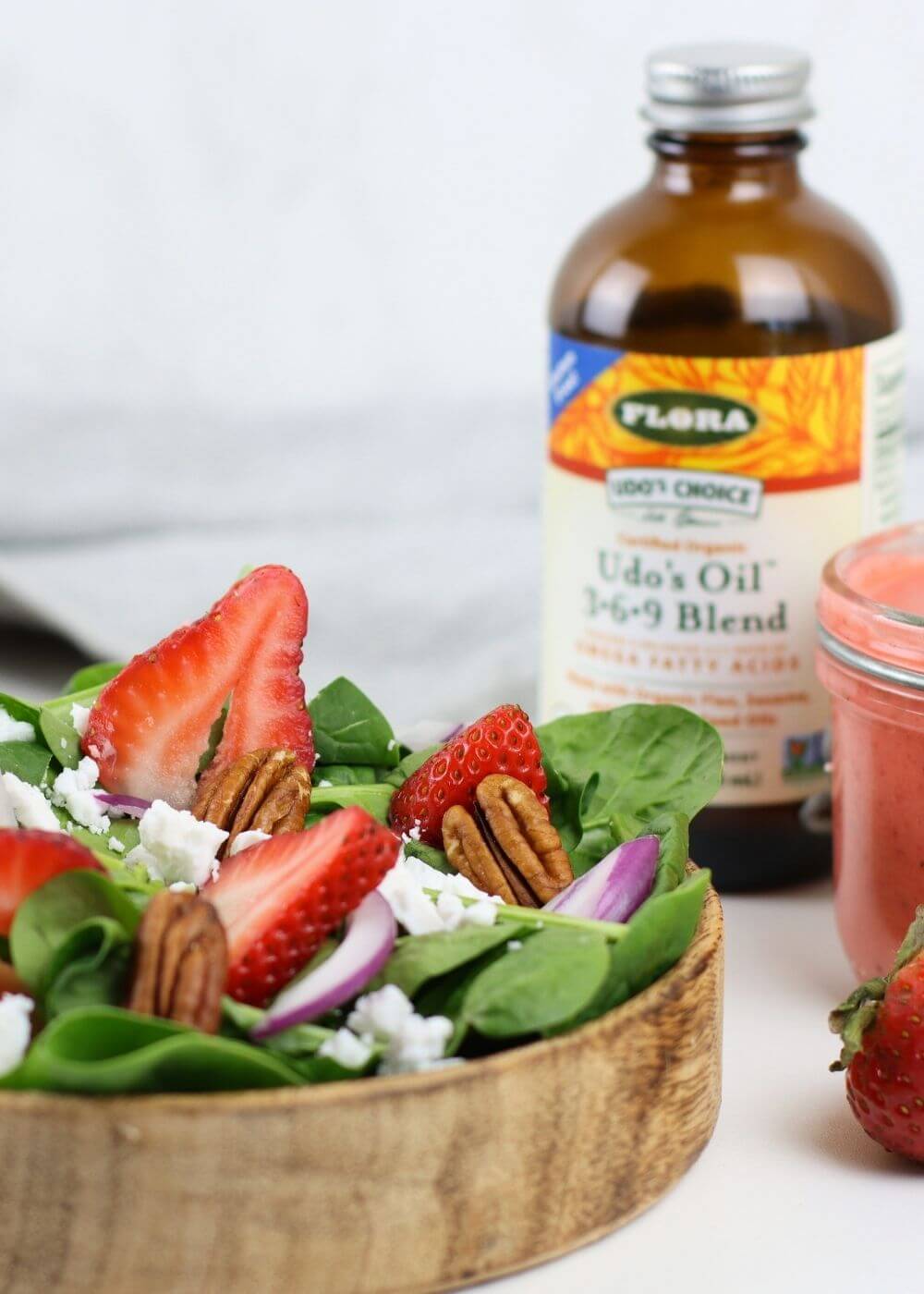 Salad with strawberries and pecans next to a bottle of Flora oil blend on a white background
