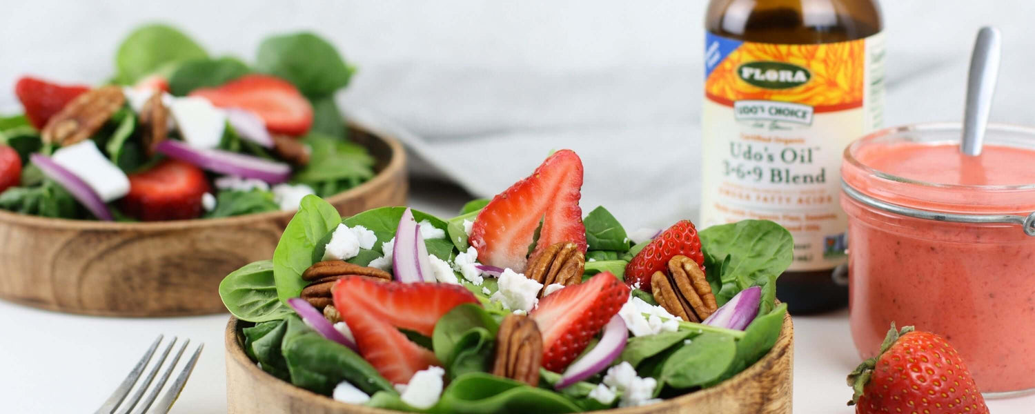 Salad with strawberries, nuts, and cheese in a wooden bowl, with a bottle of Flora oil in the background.